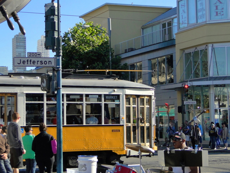 This image captures a vibrant scene from the Jefferson Street Trolley Car ride, a classic and popular mode of transportation in San Francisco. The tram is moving down the street with people waiting at the stop and buildings lining the route. The weather appears to be sunny, making it a pleasant day for sightseeing. This scene represents a typical day in the city, with locals and tourists alike enjoying the convenience and charm of the trolley system. DSC08772.JPG