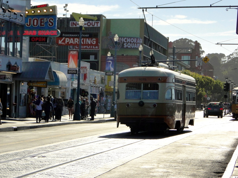 The image captures a serene moment on a city street, where a vintage trolley train is in motion. The train, painted in a classic shade of green, adds a touch of nostalgia to the urban landscape. It's passing by a bustling scene at a corner where people are going about their day. The clear sky and calmness suggest it might be early morning or late afternoon, a time when the city seems to slow down just for a moment before the hustle and bustle resumes. DSC08778.JPG