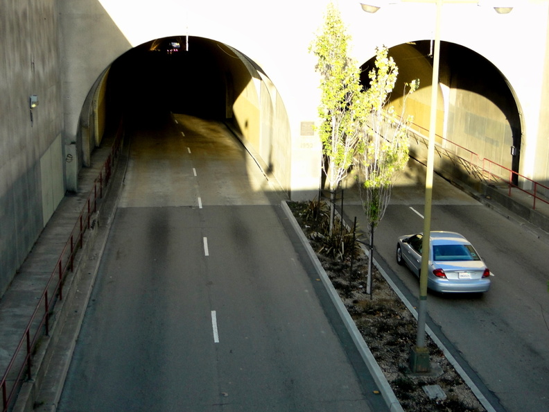 This image captures a tranquil moment in San Francisco, USA. A small car is seen making its way through a tunnel under an overcast sky. The tunnel, possibly an underground parking garage or a bypass, is bathed in natural light filtering through the large arched entrance. Surrounding the tunnel are trees and sidewalks, hinting at the urban landscape that exists beyond this secluded passageway. DSC08915.JPG