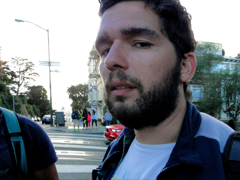 In this image, two young men are captured on a street corner in the city of San Francisco. They seem to be enjoying their time together, possibly waiting for something or someone. One individual is looking directly at the camera with an intent gaze, while the other appears to be looking towards the right side of the photo. DSC08875.JPG