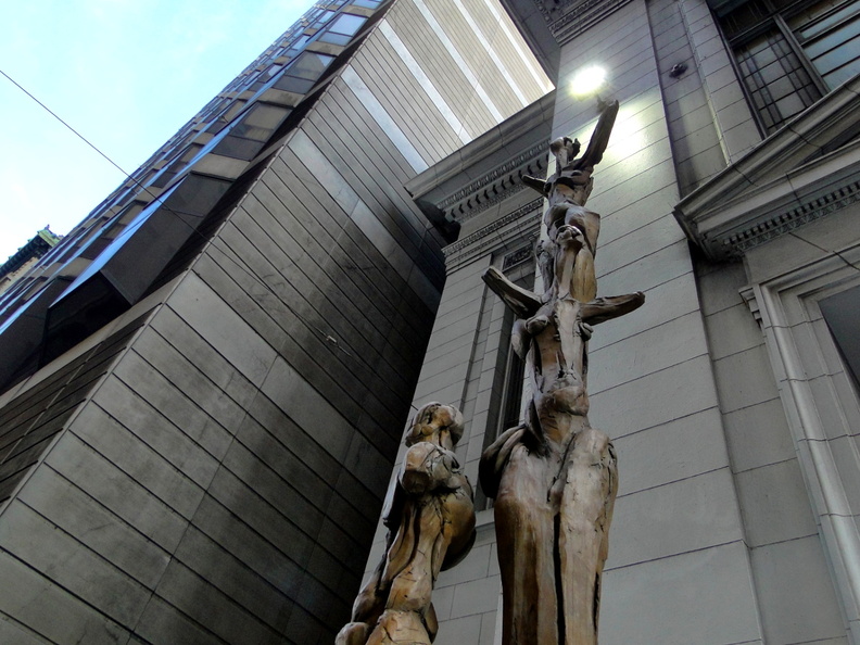 This image captures an intriguing blend of urban architecture and street art. A sculpture composed of abstract shapes and figures is prominently displayed on the facade of a building, adding a unique visual element to the cityscape. The artwork seems to interact with its surroundings, possibly commenting on the human condition or the nature of urban life. The graffiti adds an element of vandalism or perhaps intentional artistic expression, creating a dynamic and engaging scene. DSC08967.JPG