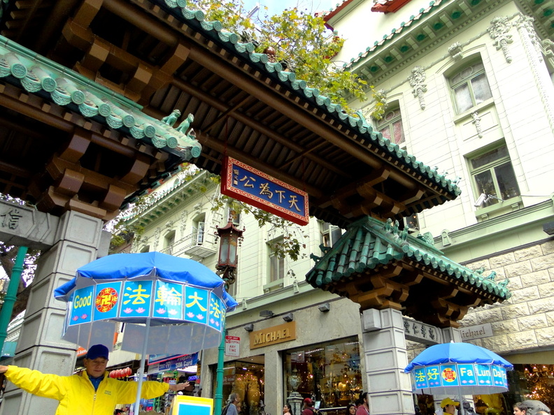 This image captures a vibrant scene from a traditional Chinese market in the heart of San Francisco. The market entrance is marked by ornate wooden beams and green roofs, adorned with intricate designs and characters that add to the cultural charm of the area. A sign bearing Asian script stands proudly above the archway, guiding visitors to this bustling hub of commerce. Vendors can be seen in action, with one vendor standing out by holding an umbrella in a picturesque setting. The backdrop showcases the architectural style of a building that complements the market's aesthetic appeal. This image beautifully encapsulates the rich heritage and lively atmosphere of San Francisco's Chinatown. DSC09072.JPG