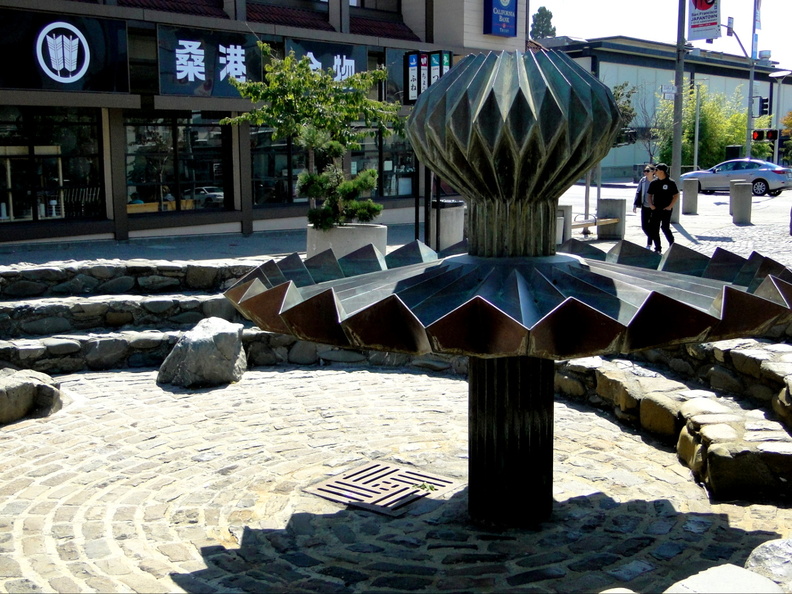 A serene and well-maintained city park featuring a central fountain with decorative elements, surrounded by lush greenery. DSC09456.JPG