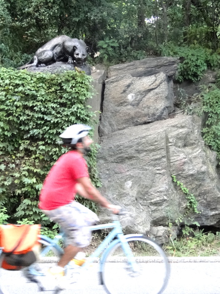 Enjoying the Outdoors: Cyclist Riding by a Sculpture of a Bear on a Rocky Bluff