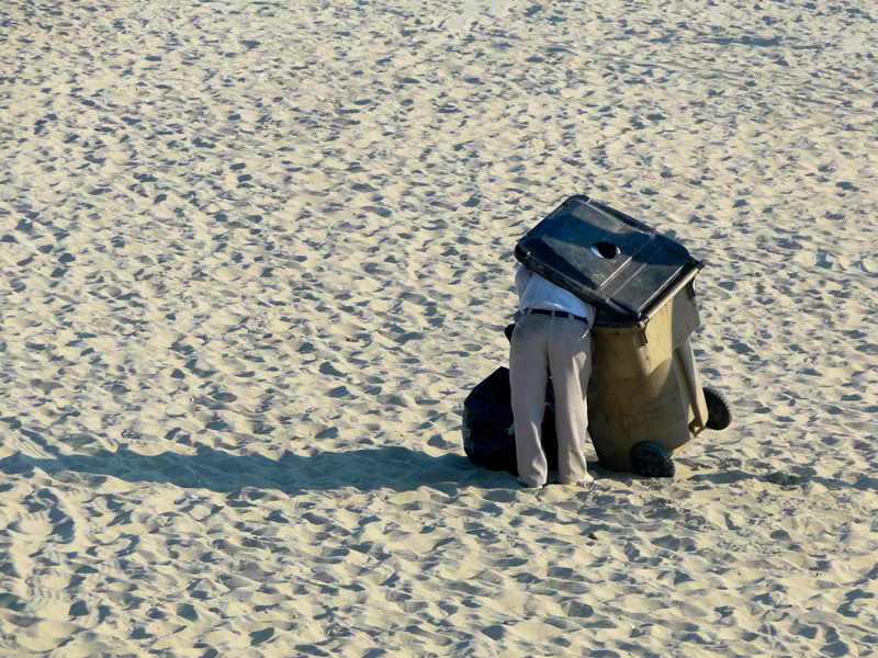 A Sanitation Worker Emptying a Trash Can on the Beach
