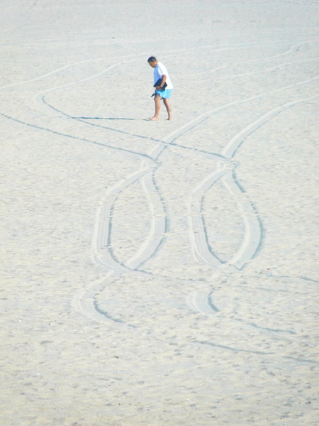 A Lone Figure on a Beach with Tire Marks