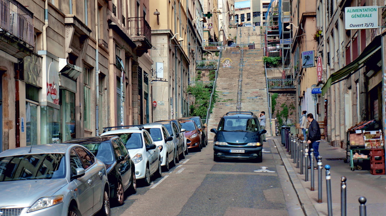 Narrow European City Street with Cars and Pedestrians