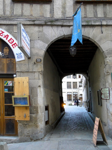 Limoges, France: A Narrow Alley Leads to a Stone Bridge Archway with Blue Flag and Signs