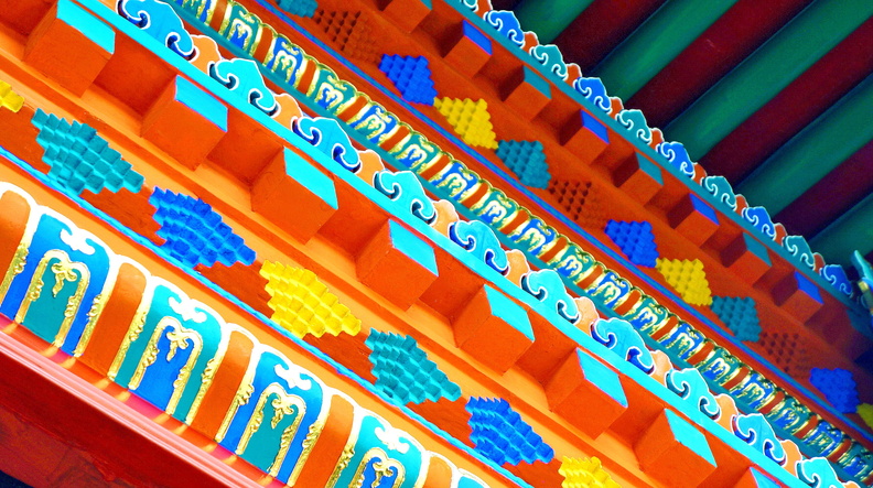 The image showcases the rich interior of an Asian temple. The walls are adorned with intricate patterns, predominantly in shades of red and blue, creating a striking contrast against the white ceiling. Colorful tiles with geometric designs add to the visual appeal. The temple's design elements are reminiscent of traditional Chinese architecture, which is further enhanced by the presence of an altar at the front. This image captures the essence of spirituality and cultural heritage found in such spaces. DSC07638.JPG