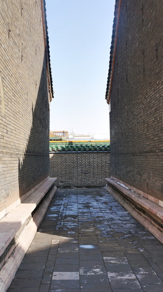 This image captures a serene, narrow alleyway in Shenyang, China. The perspective is from the end of the alley, looking towards the entrance. The brick walls on either side exhibit signs of weathering and age, typical of traditional Chinese architecture. A clear blue sky forms the backdrop, providing a peaceful atmosphere to this urban scene. This alleyway serves as a quiet respite amidst the bustling city life. DSC07667.JPG