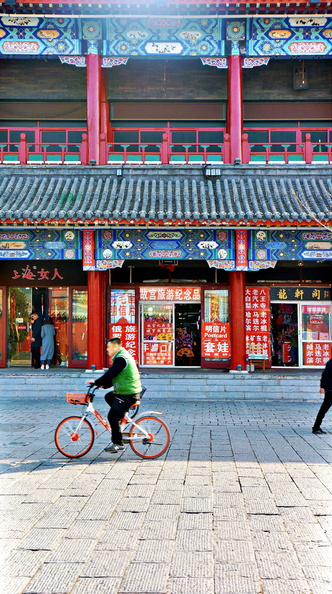 This image captures a serene moment on the streets of Shenyang, China. A cyclist is riding down an alleyway that is lined with traditional Chinese buildings featuring vibrant red accents and ornate detailing. The architecture showcases elements of East Asian culture and design. The city's atmosphere is peaceful yet lively, a snapshot of everyday life in this bustling metropolis. DSC07732.JPG