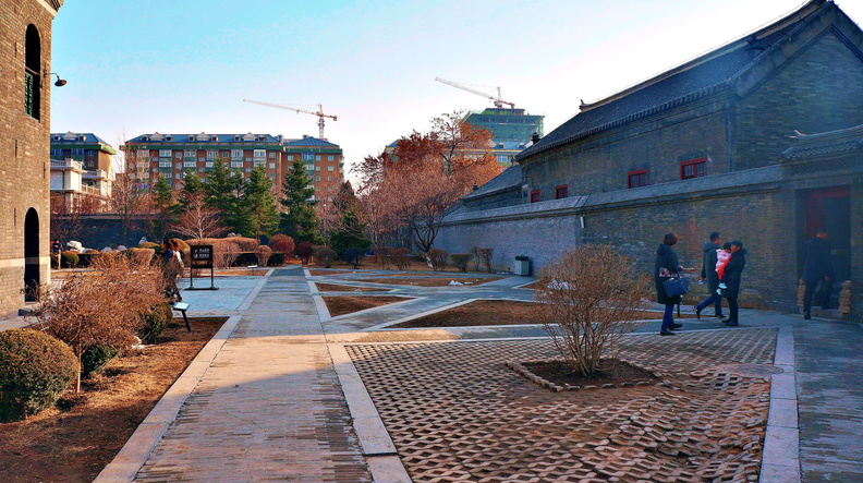 The image showcases a serene courtyard in Shenyang, China. The scene captures the tranquil ambiance of the location with its well-maintained stone paving, lush trees, and the presence of people enjoying the outdoor space. DSC07817.JPG