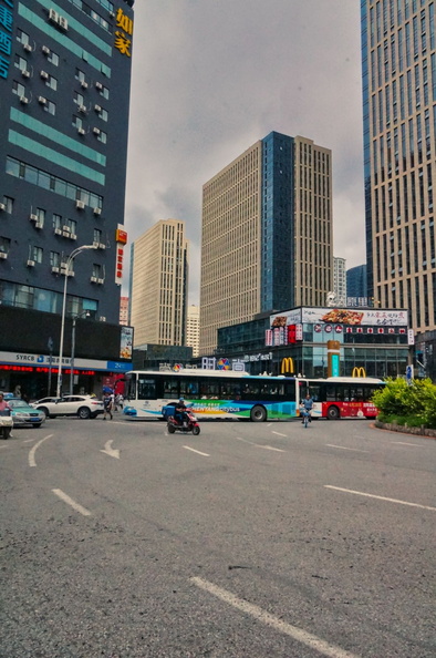 This image captures the bustling city life of Shenyang, China. The urban landscape is dominated by tall skyscrapers and a busy intersection with traffic and public transportation such as buses. The overcast sky adds a dramatic touch to the scene. DSC00911.jpg