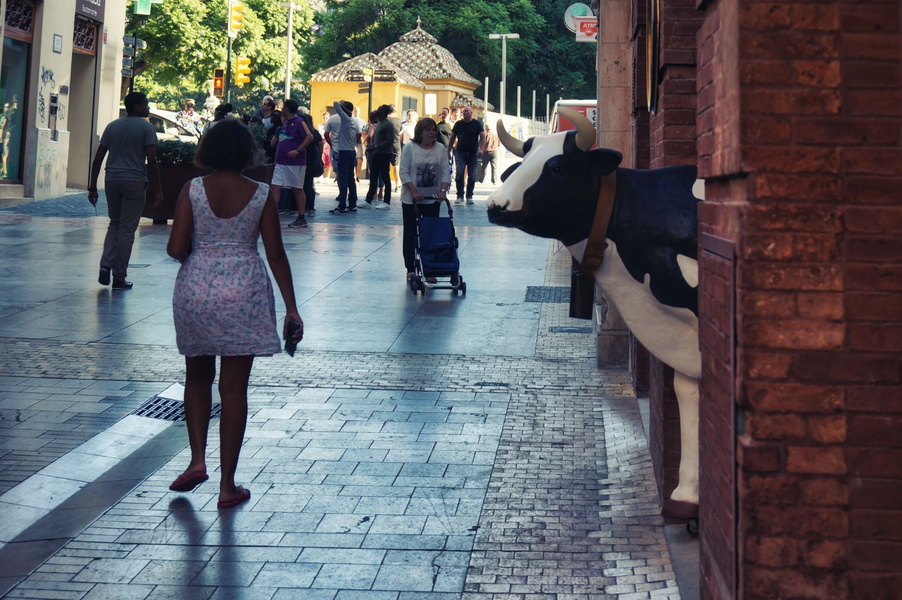 A Moment in a Busy City: A Woman Walks Past a Cow Statue in a Malagueñ Shopping Area