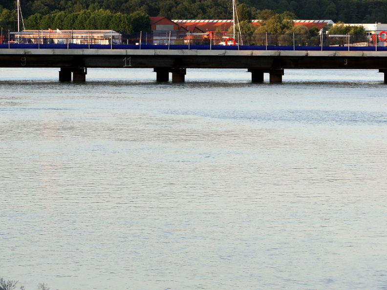 This image captures the serene beauty of a small river under a bridge, with the gentle flow of the water creating a peaceful atmosphere. The bridge appears to be in good condition and is set against the backdrop of a clear sky, adding to the idyllic setting. In the distance, you can see what looks like a train passing on elevated tracks, suggesting that this picturesque scene might be near a railway line, providing a connection between rural areas and other parts of the country. DSC03503.JPG