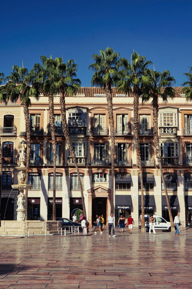 The image depicts a lively street scene in the heart of Malaga, Spain. The courtyard is characterized by its Spanish-style building, complete with balconies that offer a vantage point overlooking streets. A few palm trees add to the tropical ambiance of the location. The area appears to be a popular destination for tourists, as evidenced by several people exploring the surroundings. This picturesque corner of Malaga showcases the city's blend of historical charm and modern-day activity. DSC01133.jpg