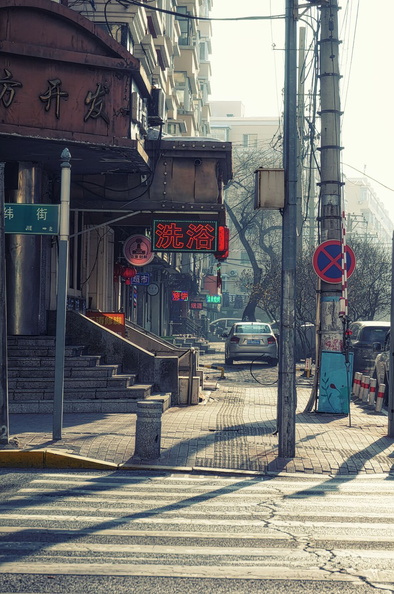 This image captures a typical day on a city street in Asia. The scene features a commercial district with various shops and restaurants, as indicated by the visible signs. A pedestrian crosswalk suggests it's a pedestrian-friendly area. There is public transportation evident in the form of a bus stop. The architecture has an Asian design style, contributing to the overall ambiance of the locale. DSC05047.jpg